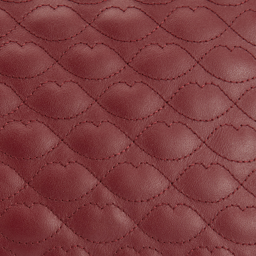 Close-up of a quilted burgundy leather texture with lip-shaped stitching.
