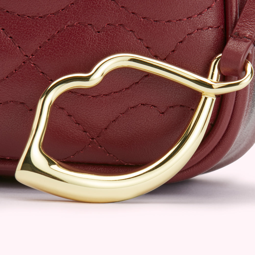 Close-up of a burgundy quilted leather handbag with a gold lip-shaped clasp.
