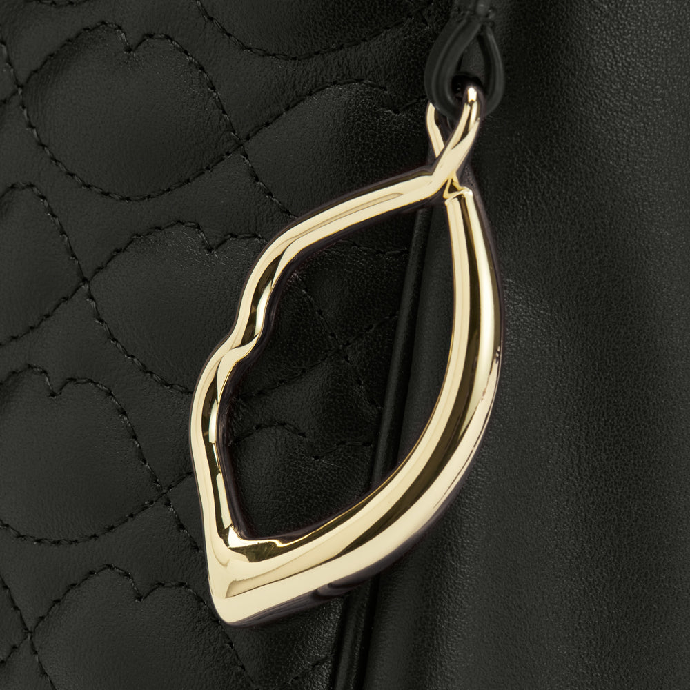 Close-up of a gold lip-shaped detail on a black quilted leather bag.
