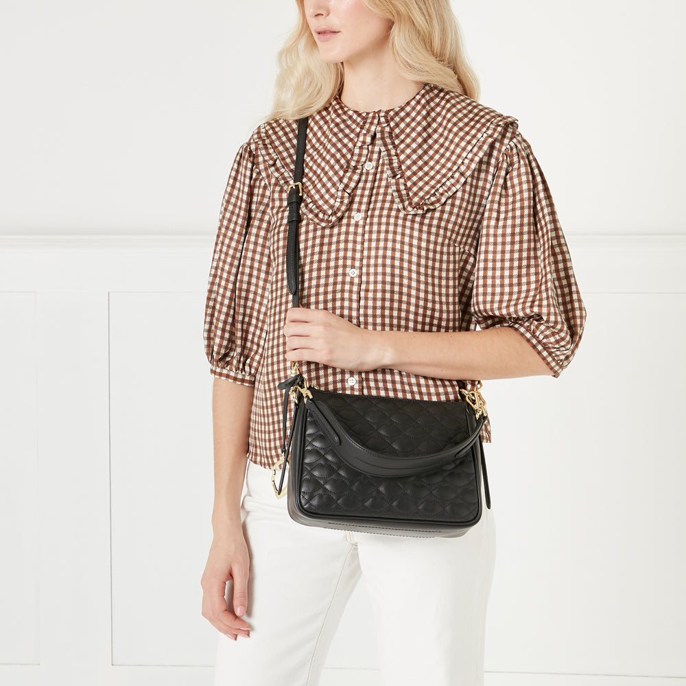Model wearing a black quilted crossbody bag against a white background.