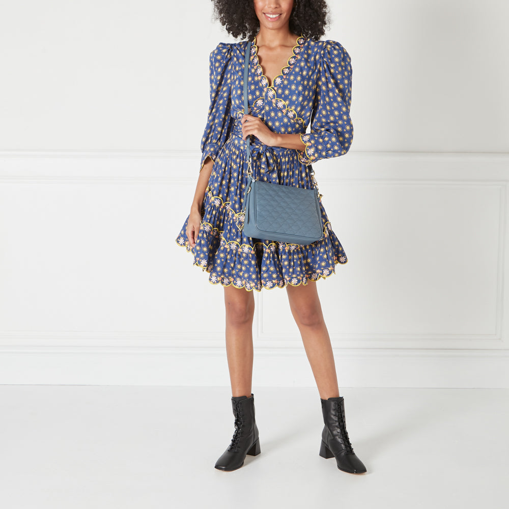 A woman in a blue floral dress and black boots is modelling a light blue quilted crossbody bag.