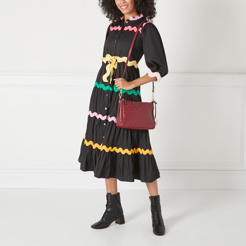 A woman in a black and colourful dress carries a dark red quilted crossbody bag.
