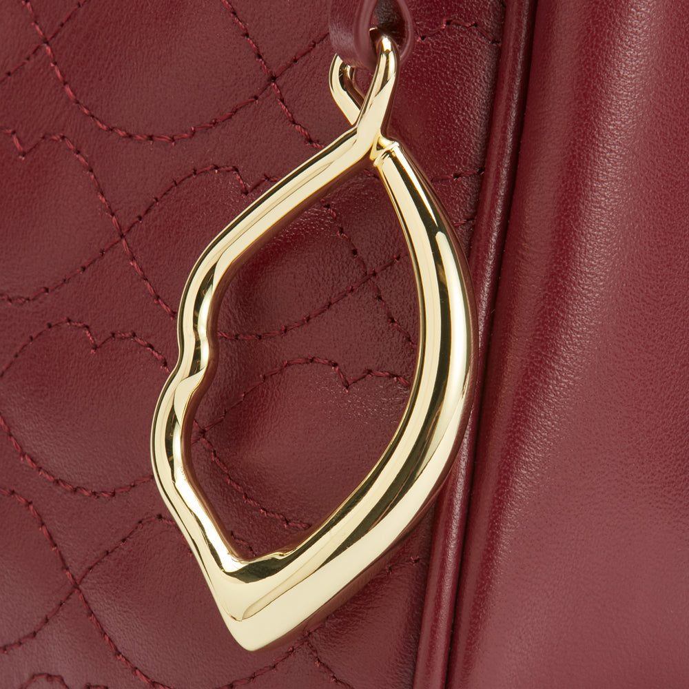 Close-up of a burgundy quilted leather handbag with a gold lip-shaped charm.