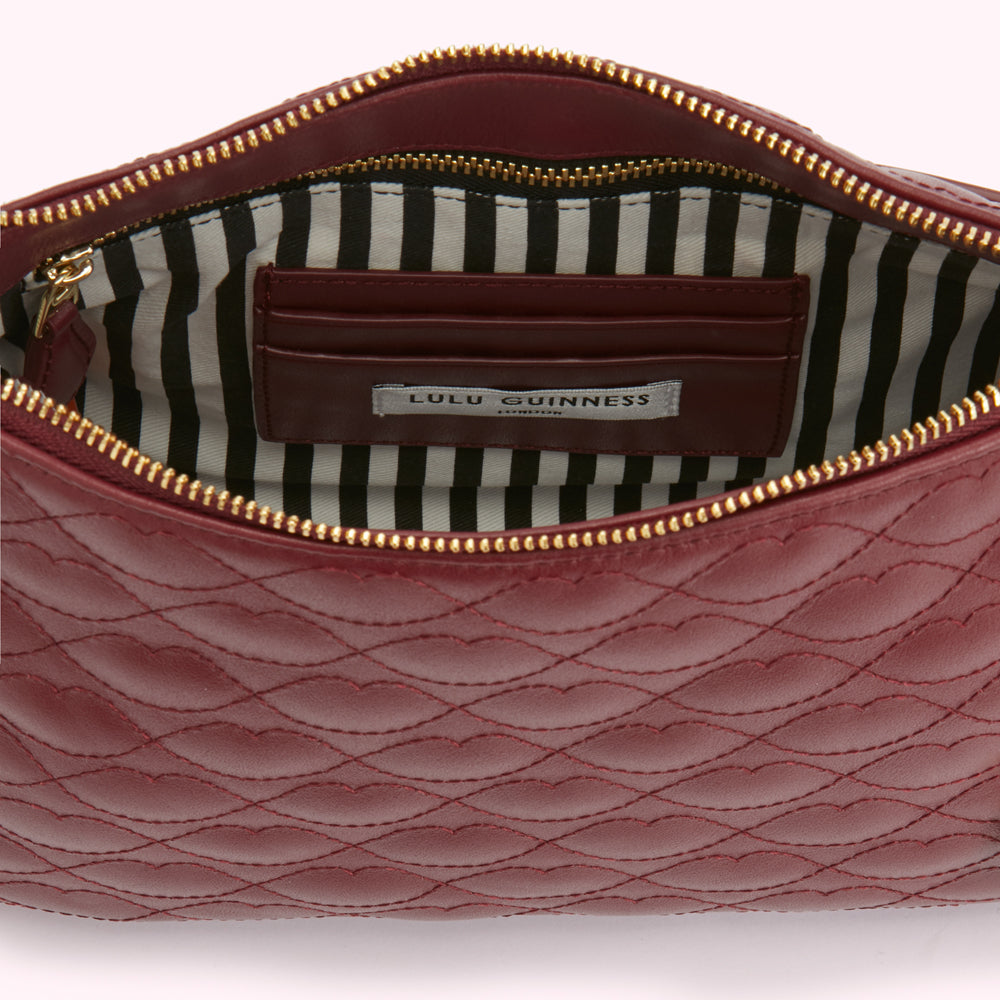 Interior view of a burgundy quilted Lulu Guinness purse with a gold zipper and black and white striped lining.