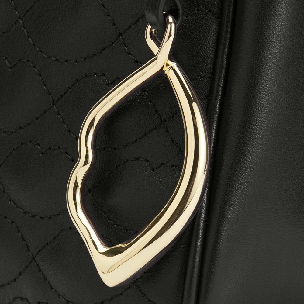 Close-up of a gold lip-shaped charm attached to a black quilted leather bag.
