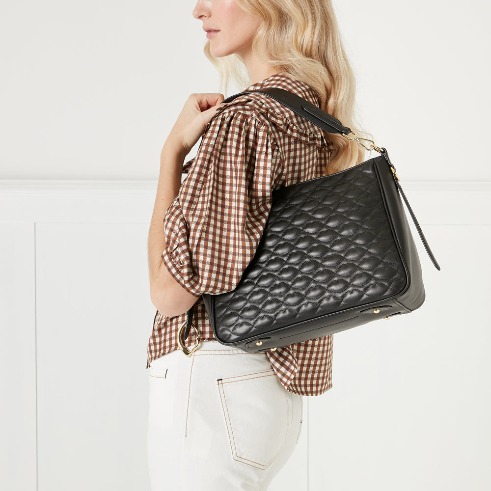 Woman holding a black quilted leather shoulder bag against a white background.
