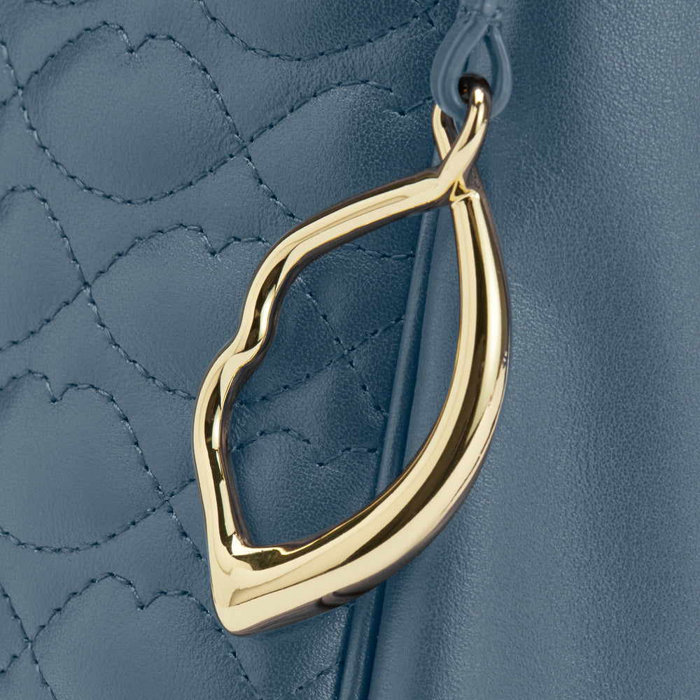 Close-up of a blue quilted leather handbag with a gold lip-shaped clasp.
