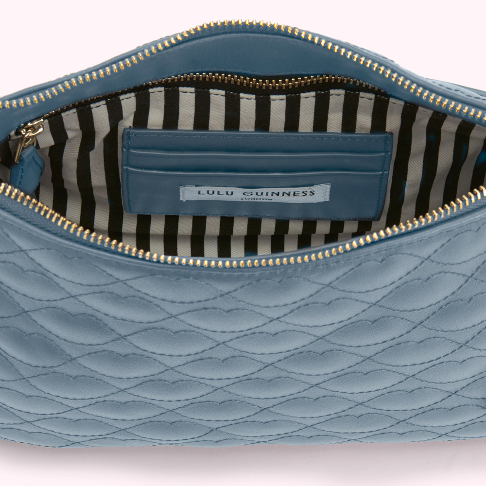 Interior of a blue Lulu Guinness quilted leather clutch open to reveal a black and white striped lining and a matching blue internal pocket.