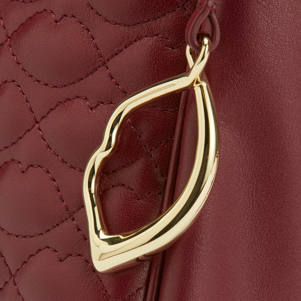 Close-up of a burgundy quilted leather handbag with a gold lip-shaped zipper pull.