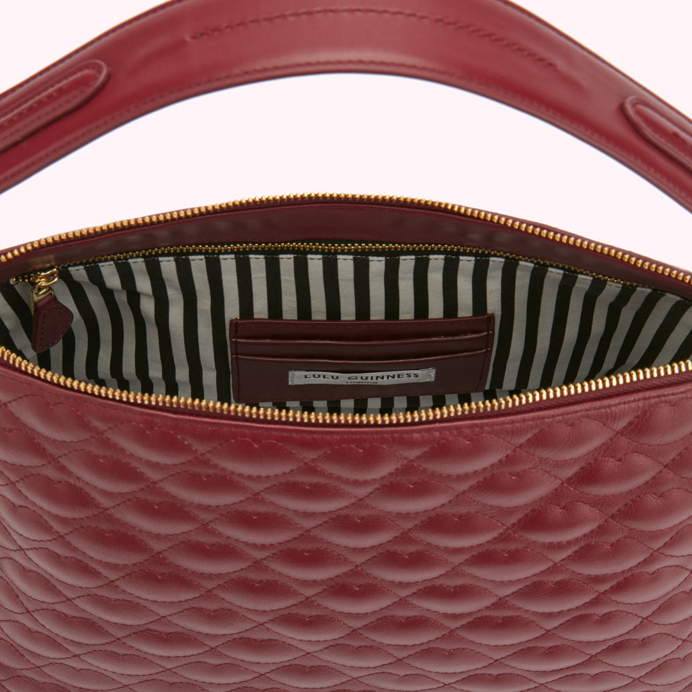 Inside view of a burgundy quilted Lulu Guinness handbag with a gold zipper and black and white striped lining.