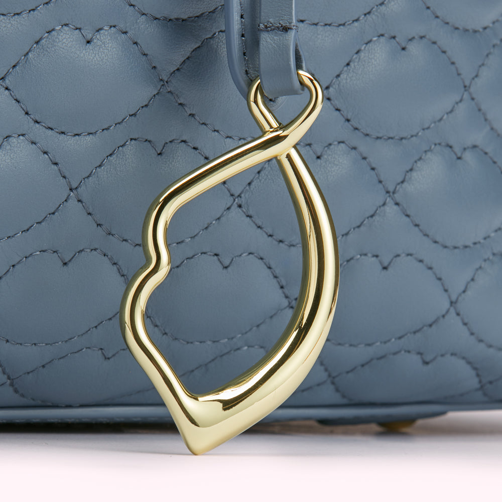 Close-up of a gold-coloured lip-shaped detail on a powder blue quilted leather bag.