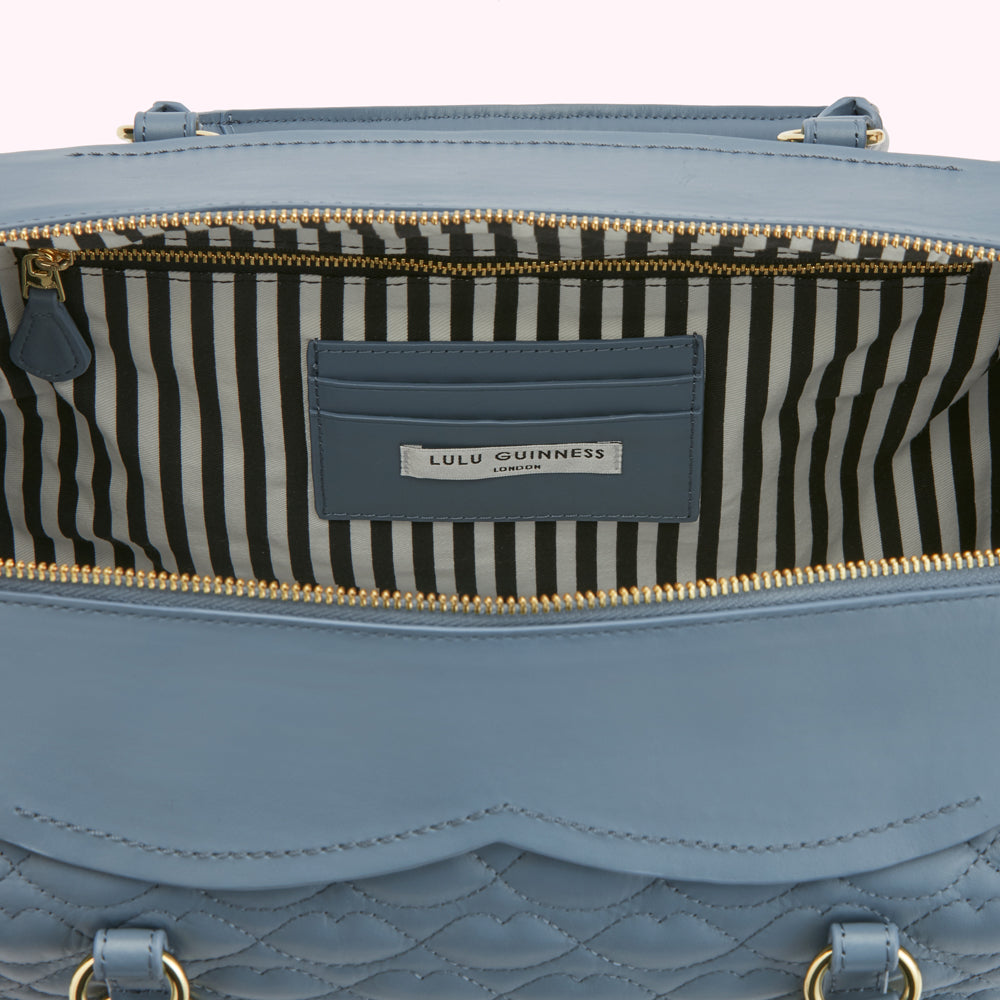 Interior of a dusty blue Lulu Guinness London quilted handbag showing the black and white striped lining and gold zipper.

