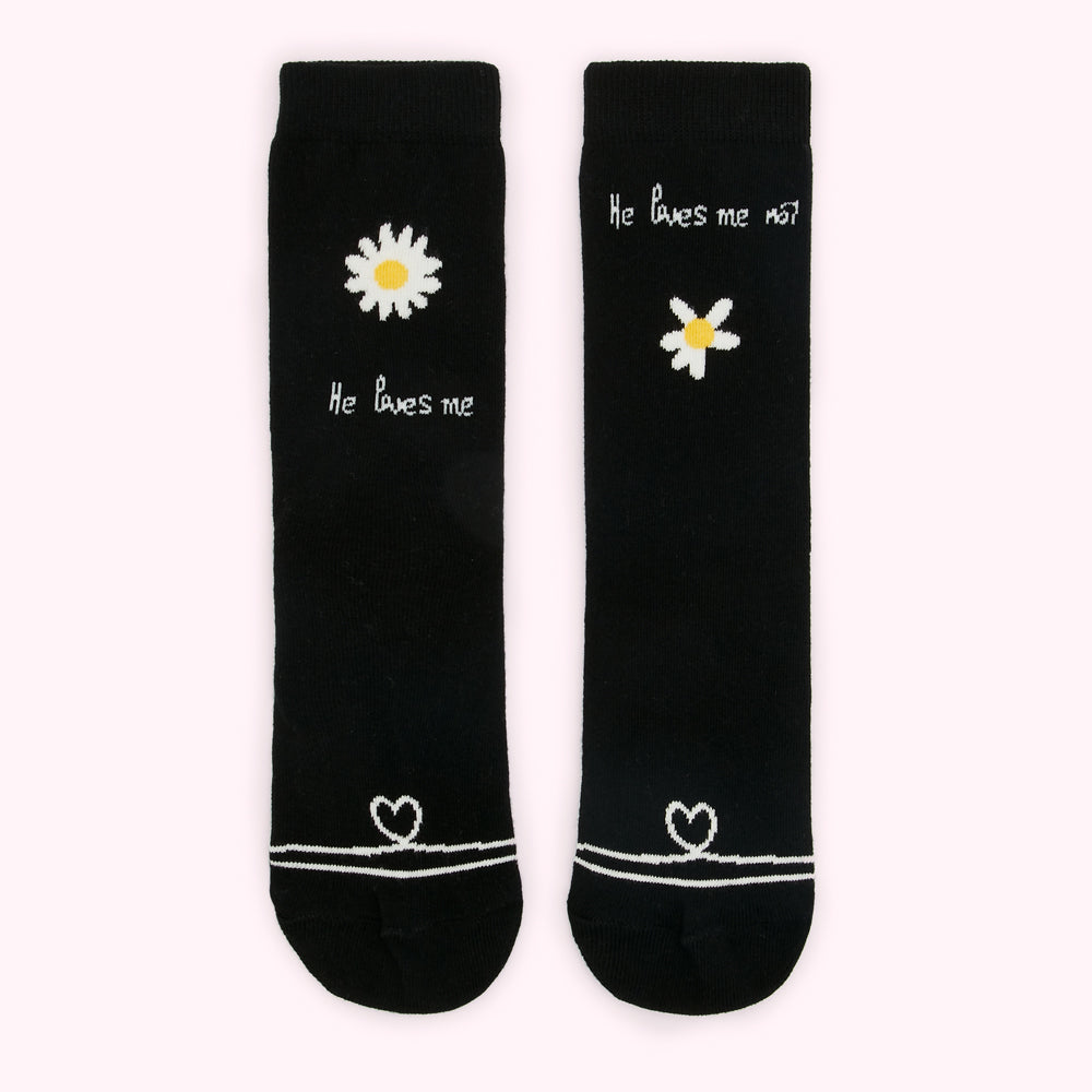 Pair of black socks with white daisy and heart designs and "He loves me" and "He loves me not" text.