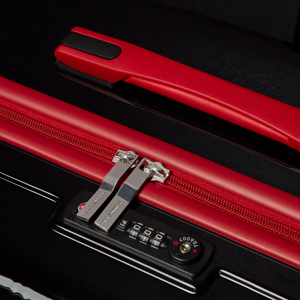 Close-up of a black and red suitcase, showcasing its TSA-approved lock and red zipper.
