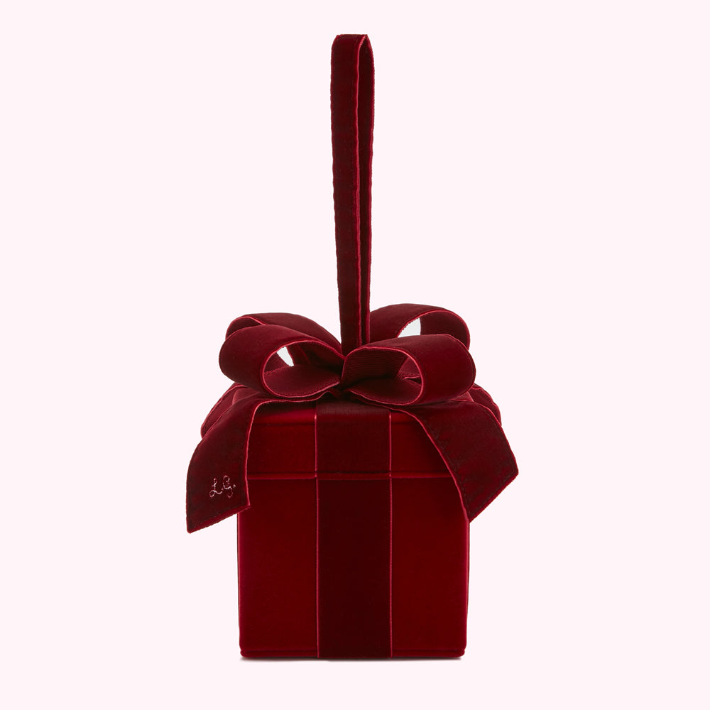 Red velvet gift box-shaped handbag with a bow and a top handle, against a white background.
