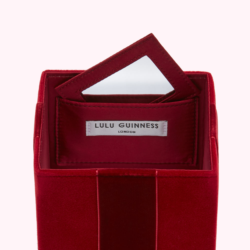Interior of a red velvet Lulu Guinness London box with a small mirror.
