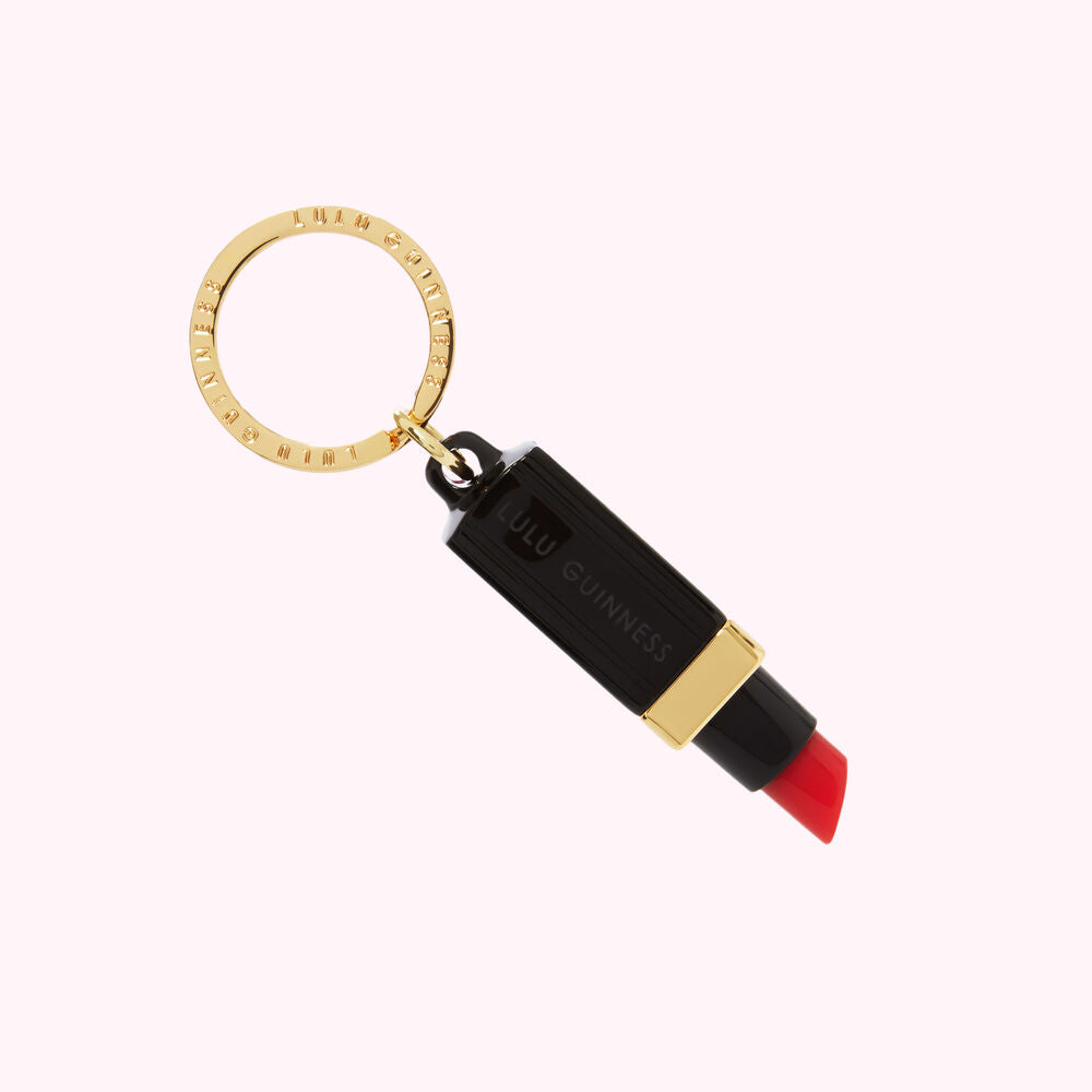 Black lipstick-shaped keychain with gold lettering and ring.
