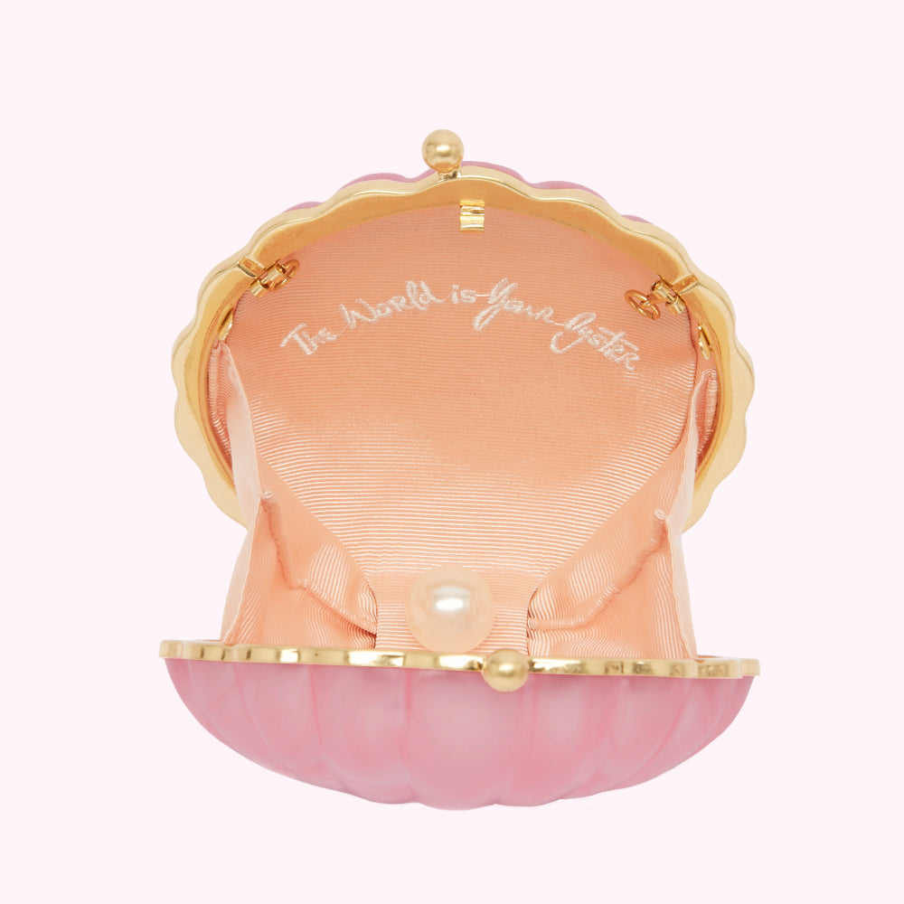 Pink seashell-shaped purse open to reveal a pale peach satin interior with a faux pearl and the words "The world is your oyster" embroidered inside.
