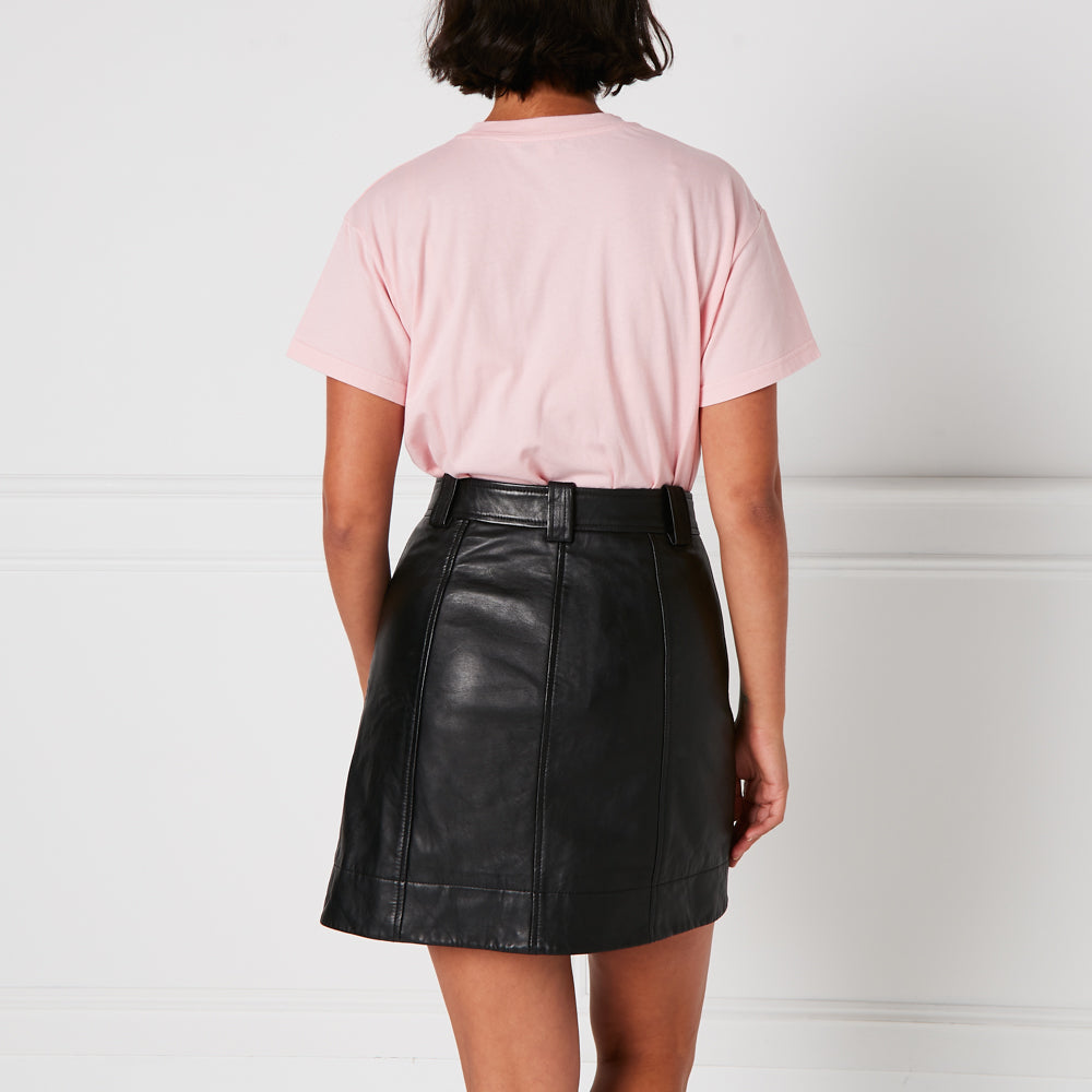 Woman from behind wearing a pink t-shirt and a black leather mini skirt against a white background.
