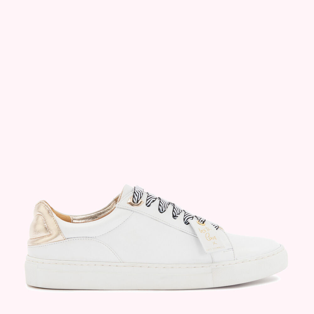White leather sneakers with gold heel detail and zebra-print laces against a pink background.

