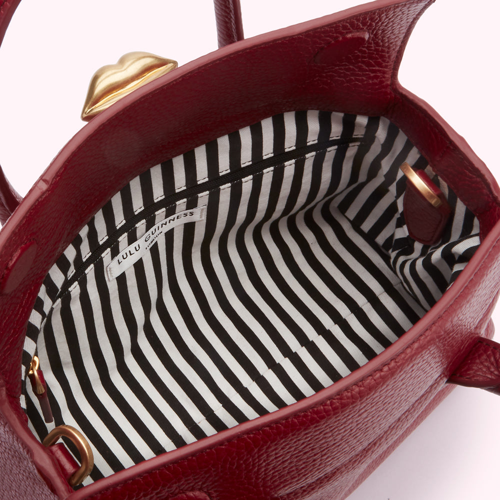 Inside of a red Lulu Guinness handbag with a black and white striped lining and a gold lip detail on the top.
