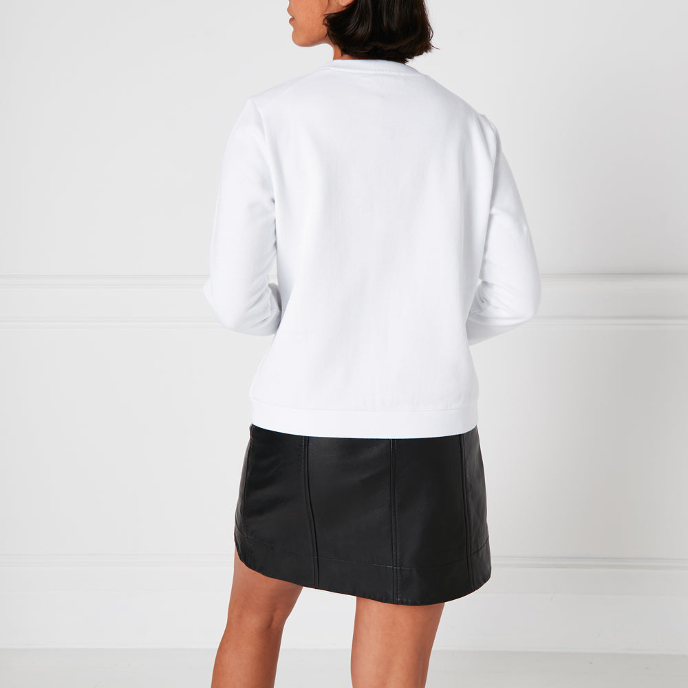 Rear view of a woman wearing a white sweatshirt and a black leather mini skirt against a white background.
