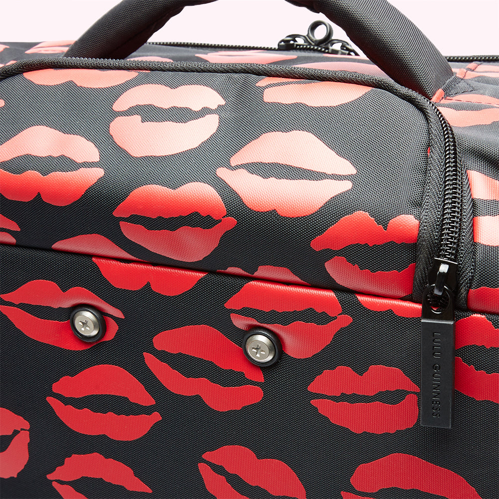 Close-up of a black Lulu Guinness travel bag with a red lips pattern.