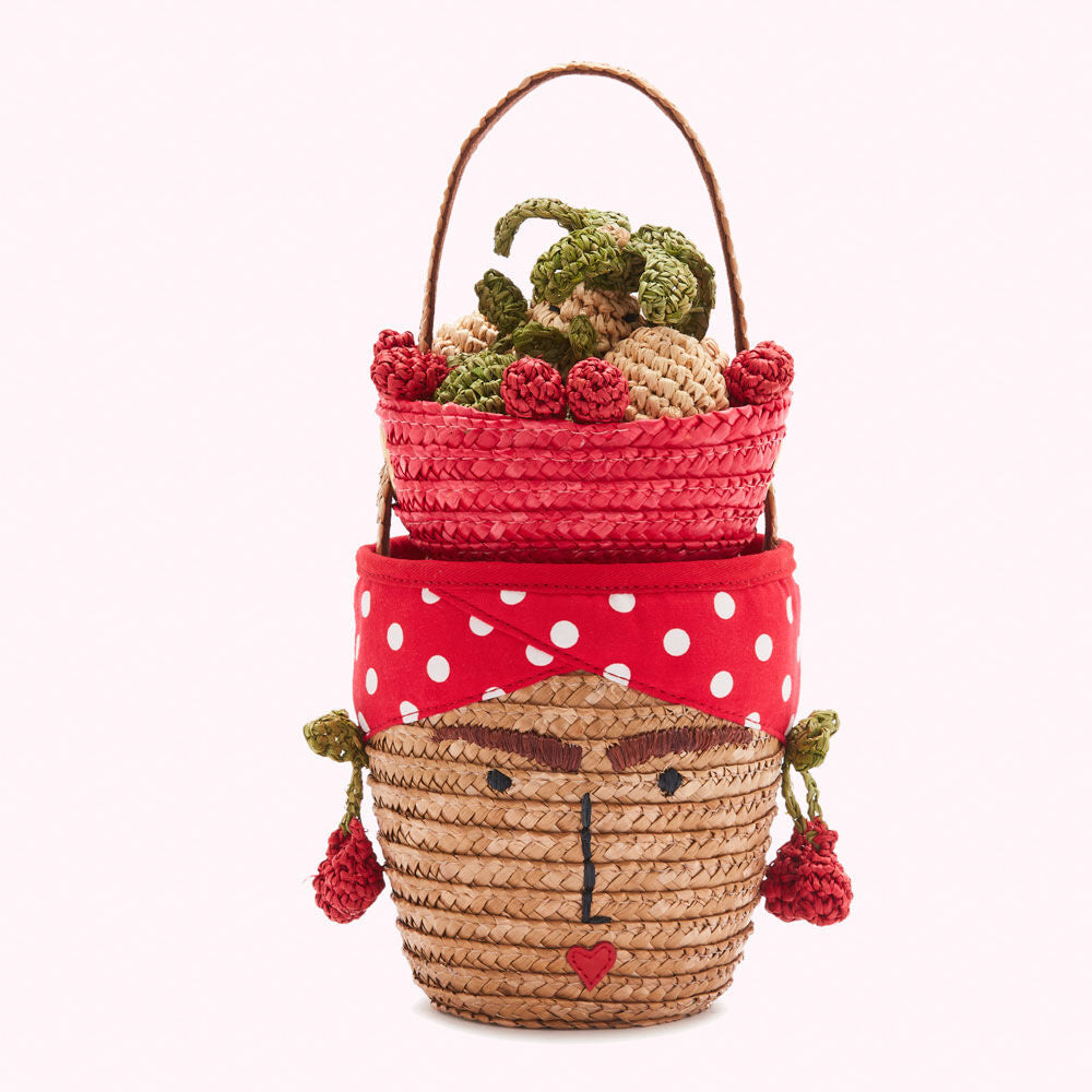 Stackable straw baskets; the top basket is red and filled with crocheted fruit; the bottom basket is decorated with a red polka dot headband and a woman's face.