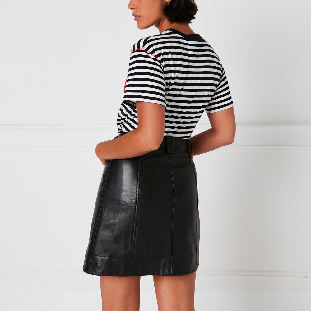 Woman from behind wearing black leather mini skirt and black and white striped shirt against a white background.
